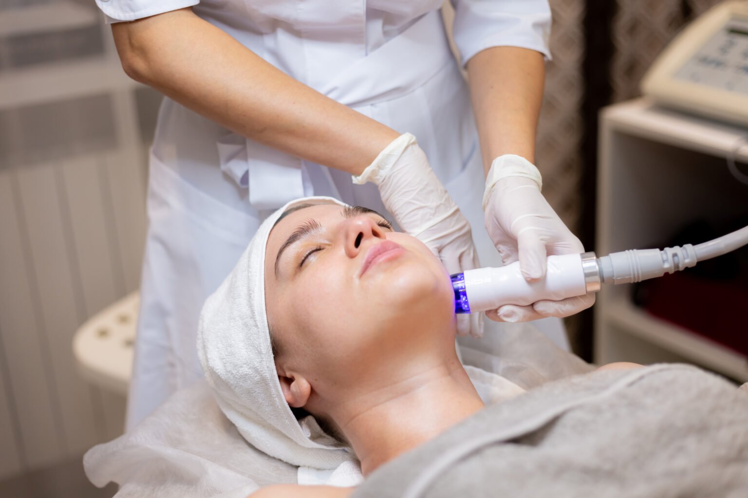 A young beautiful girl lies on the beautician's table and receives procedures with a professional apparatus for skin rejuvenation and moisturizing